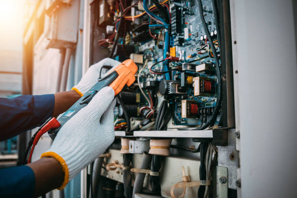 Electrician testing industrial control panel with orange digital clamp meter